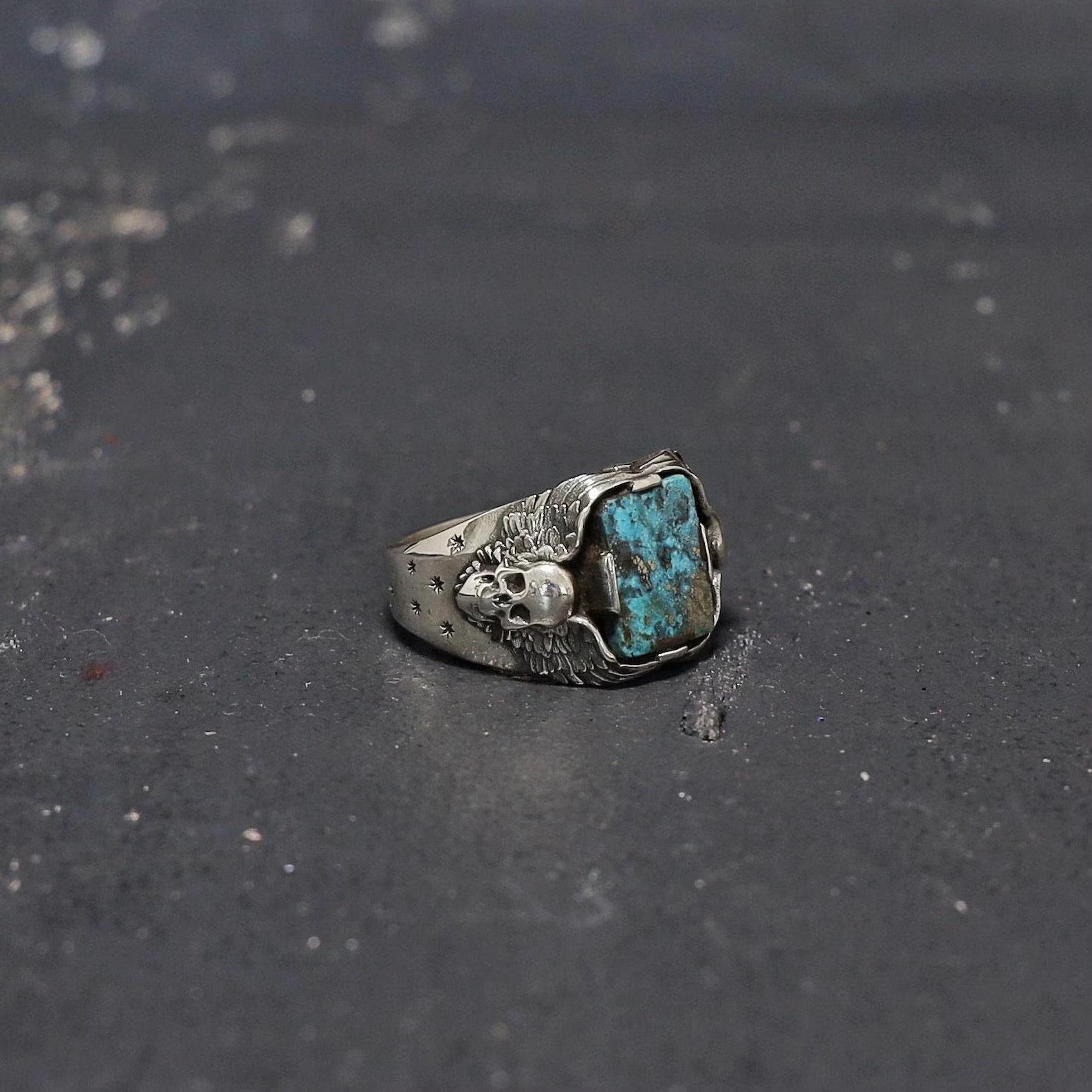 This unique men’s biker ring is a stunning blend of gothic artistry and traditional craftsmanship. Handmade from sterling silver, the ring’s centerpiece is a rough natural turquoise gemstone guarded by two fierce skulls. With a rugged texture and dark antique finish, it evokes the freedom of the open road and is an ideal gift for motorcyclists, rock enthusiasts, or fans of alternative fashion.