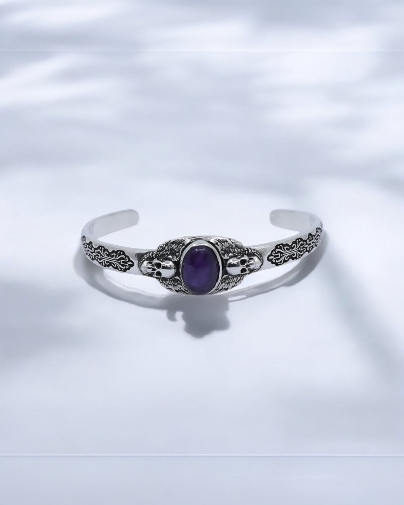 Close-up image of a handcrafted 925 sterling silver skull cuff bracelet featuring a deep purple amethyst gemstone in the center. The detailed gothic skull and wing engravings reflect premium craftsmanship and strength. Perfect for men who love handmade gothic jewelry and luxury silver accessories.