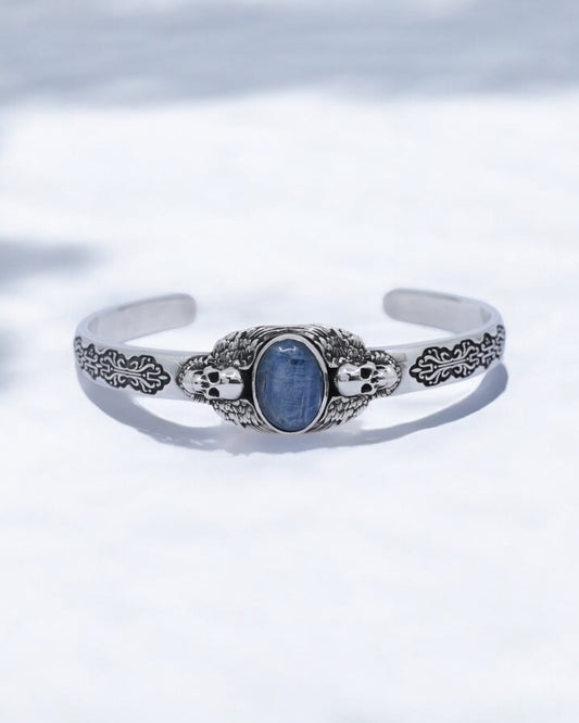 Close-up of handcrafted 925 sterling silver skull cuff bracelet featuring a natural blue kyanite gemstone in the center, surrounded by detailed gothic skull engravings and oxidized textures. Perfect for men who love handmade biker jewelry, unique gifts, and high-quality silver craftsmanship.