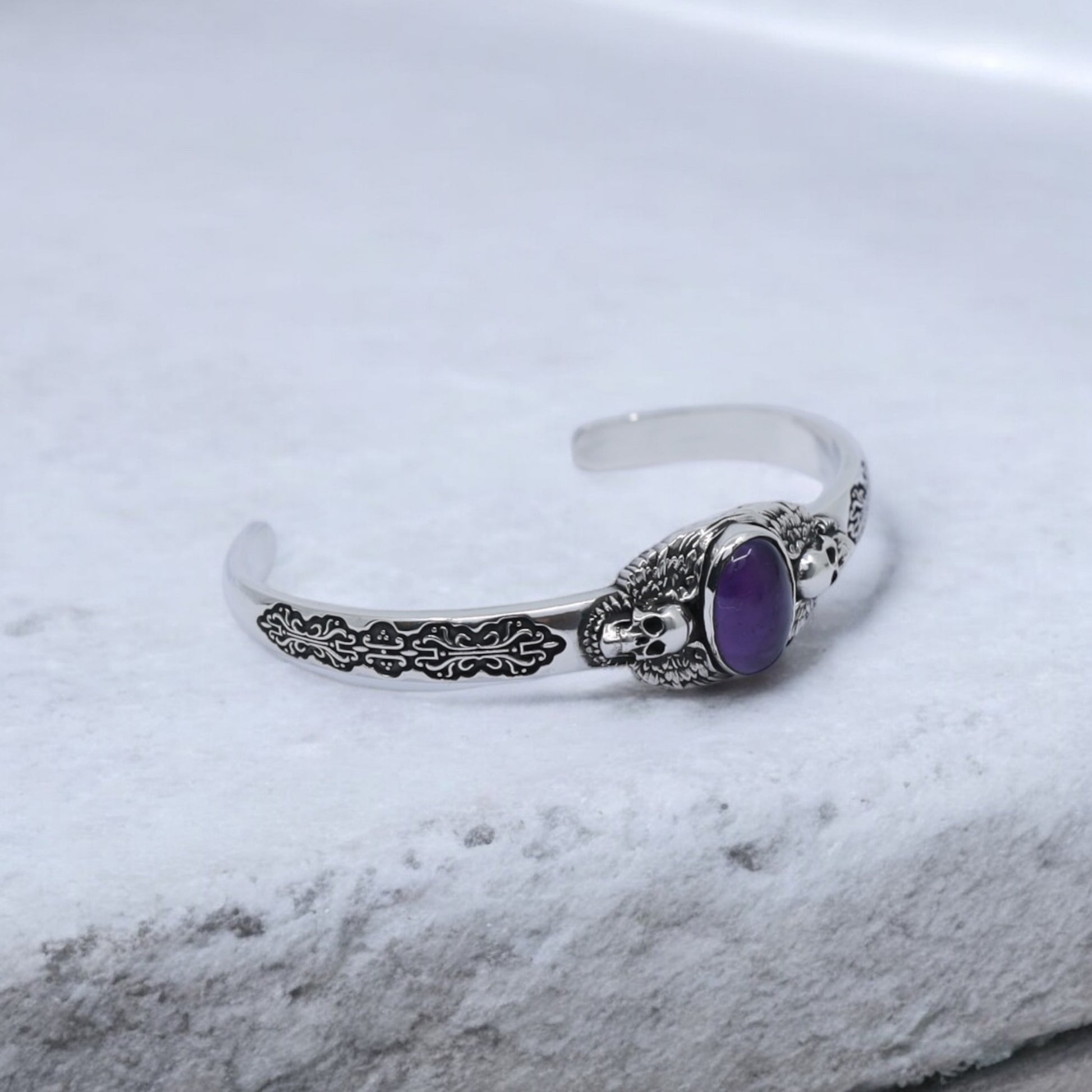 Gothic-style amethyst silver bracelet featuring two skulls and wing engravings on oxidized sterling silver. Designed for men who value individuality, craftsmanship, and unique handmade silver jewelry that makes a statement.