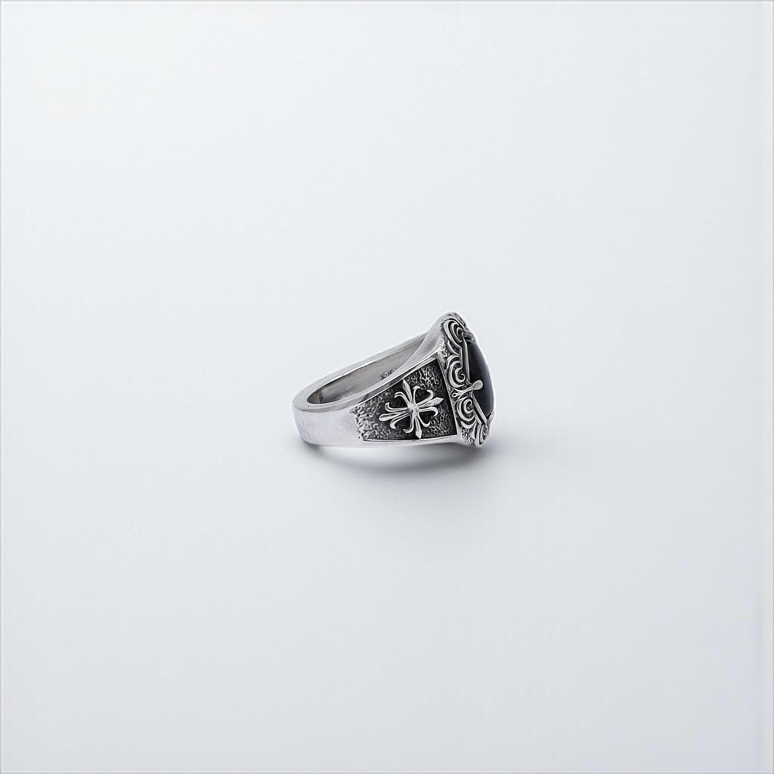 Side-angle view of a bold sterling silver men's ring with ornate gothic design, showcasing a glossy oval onyx stone and antique-style engraving—this powerful statement piece blends classic craftsmanship with modern edge, making it suitable for both everyday wear and special occasions.