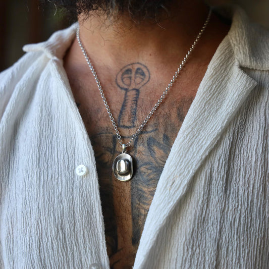 Close-up of a handcrafted sterling silver cowboy hat pendant necklace, featuring a detailed western hat charm with brushed texture, suspended on a thick silver chain and photographed against a clean white background.