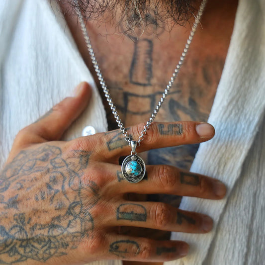 Turquoise gemstone necklace with intricate sterling silver nautical design, including hand-carved waves and a seashell emblem, photographed on a white background to emphasize the color contrast and handmade quality.