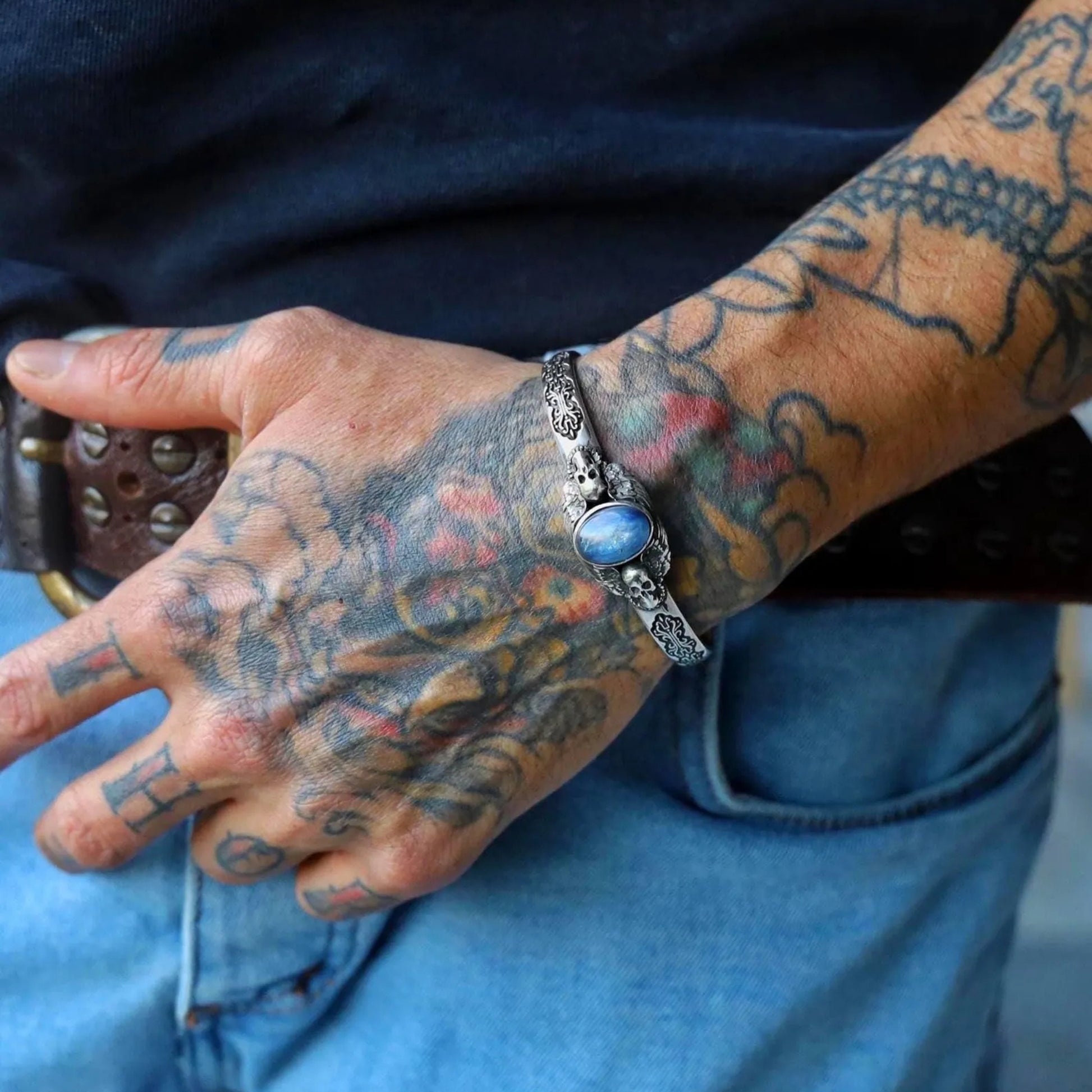 Macro shot of gothic silver cuff bracelet with skull details and blue gemstone. The oxidized 925 sterling silver adds contrast and depth, making this handmade bracelet a symbol of power, mystery, and style for men.