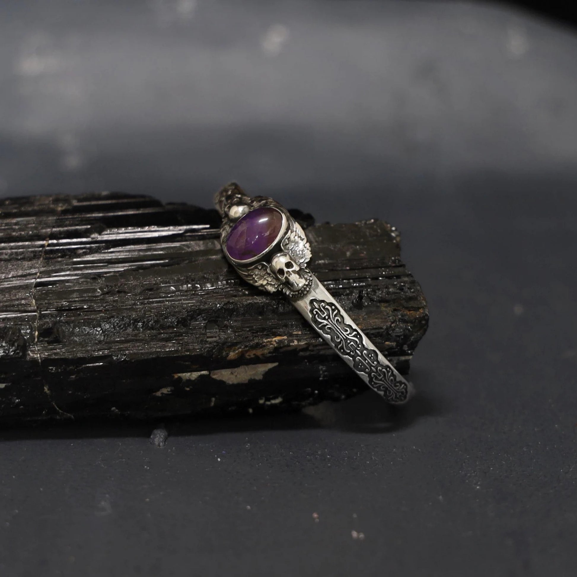 Minimal background image of a handmade sterling silver cuff bracelet featuring a genuine amethyst gemstone and twin skulls. A unique expression of gothic artistry and craftsmanship, designed for confident, stylish men.