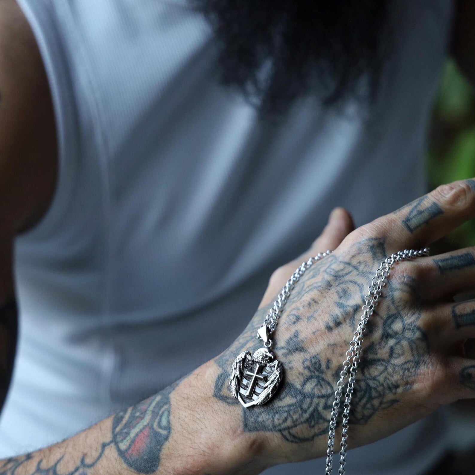 The eagle cross pendant photographed next to a motorcycle helmet and dog tags, representing strength, rebellion, and heritage. This sterling silver necklace is a favorite among men who live boldly and stand for their values. A high-quality, handcrafted necklace that’s ideal for bikers, veterans, and gothic fashion enthusiasts alike.