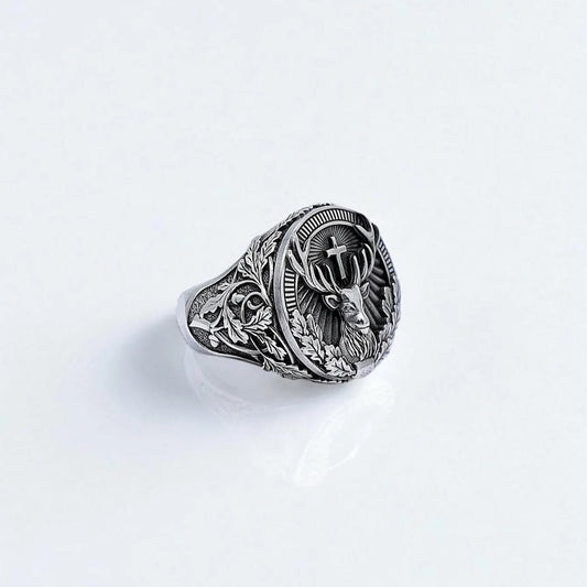 A handcrafted sterling silver ring featuring a detailed stag with a cross between its antlers, surrounded by gothic leaf engravings. The intricate front-facing design symbolizes strength, nature, and spiritual guidance, making it an ideal piece for outdoorsmen and lovers of symbolic jewelry.