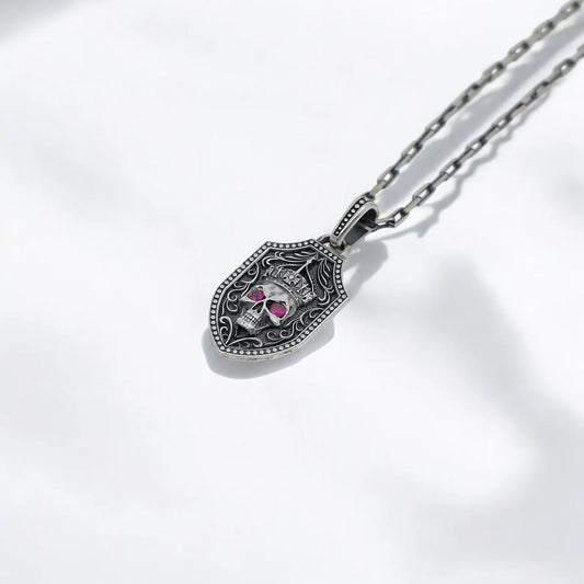 Sterling silver skull sword necklace with double-sided pendant design, featuring a crowned skull with red gemstone eyes on one side and a detailed sword engraving on the other. This handcrafted gothic shield necklace blends medieval warrior vibes with dark elegance, making it perfect for fans of Days Gone, punk fashion, and skull jewelry.