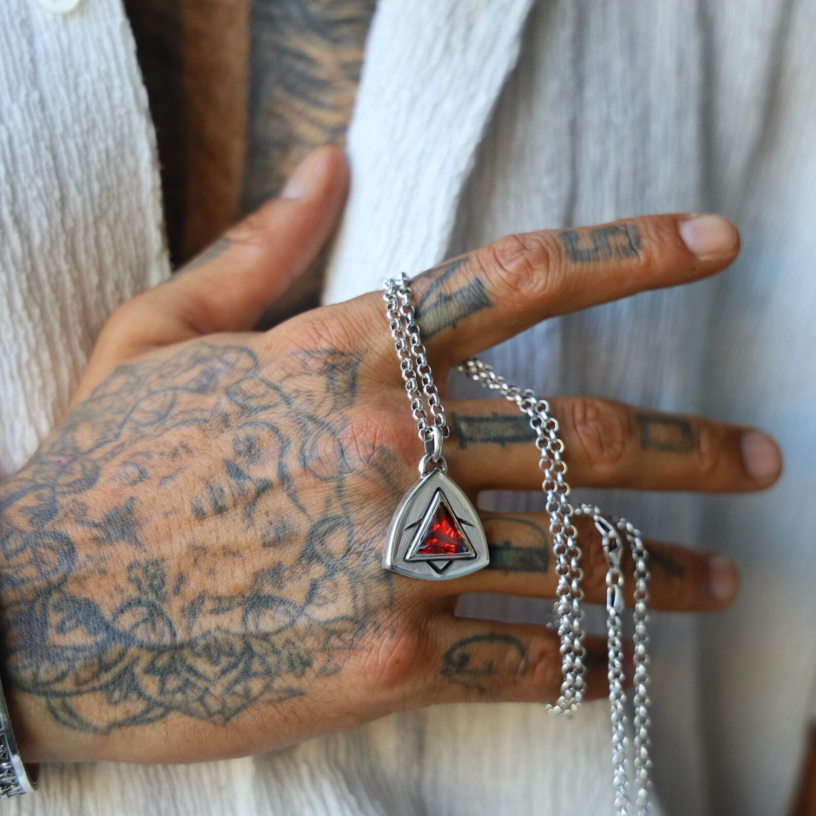 Elegant men's or unisex necklace featuring a sharp-edged triangle ruby gemstone in a heavy sterling silver bezel, symbolizing strength and precision, shot from above to emphasize the modern gothic aesthetic.