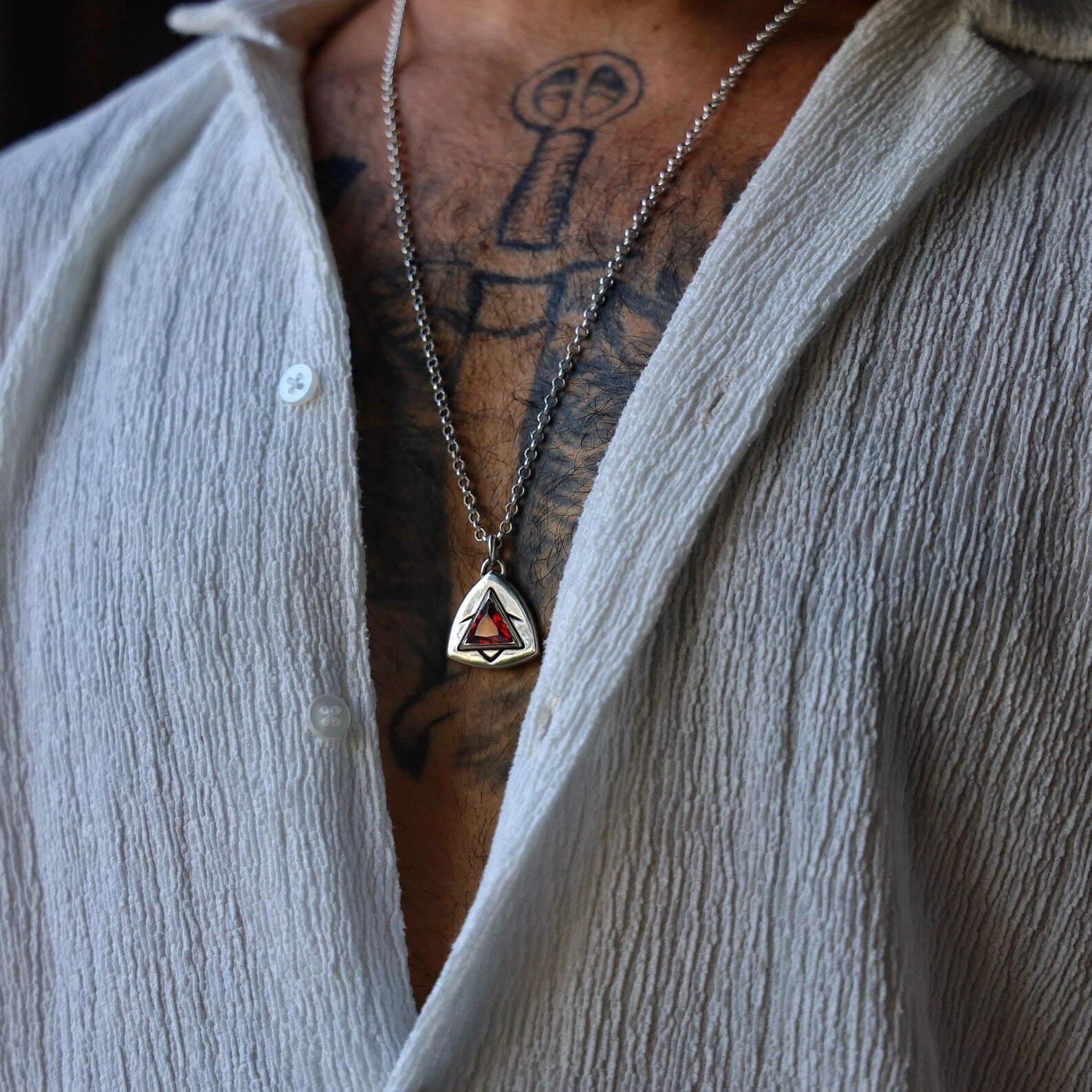 Bold and artistic handmade necklace with a triangle-cut ruby gemstone set in thick silver, styled with subtle black engraved lines for a futuristic and edgy touch, resting on a minimal background to highlight craftsmanship.