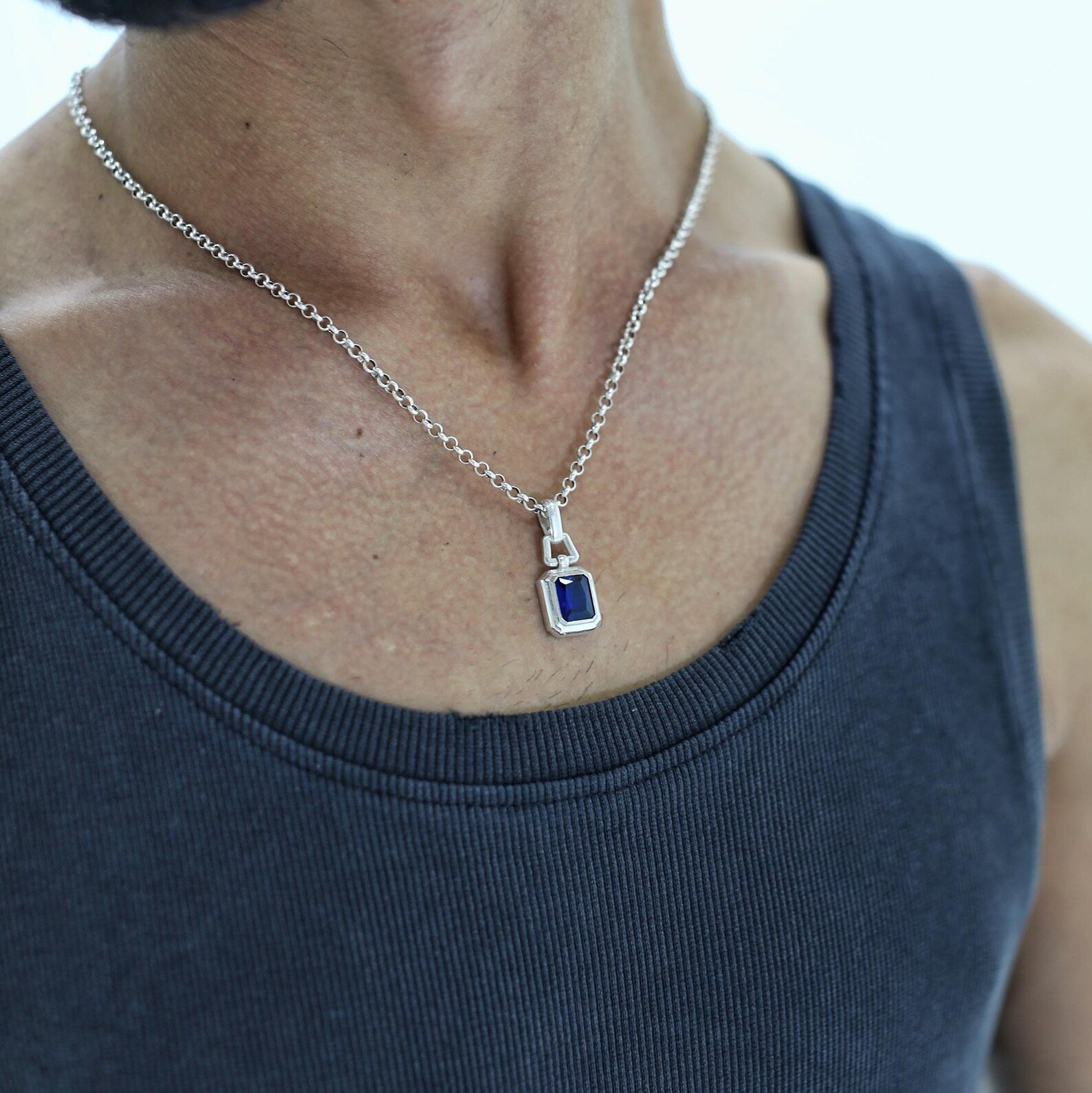 A statement necklace with an emerald-cut sapphire centerpiece set in sterling silver, crafted for men who value clean design and emotional depth. This piece blends strength and beauty, offering a personalized option through custom engraving.