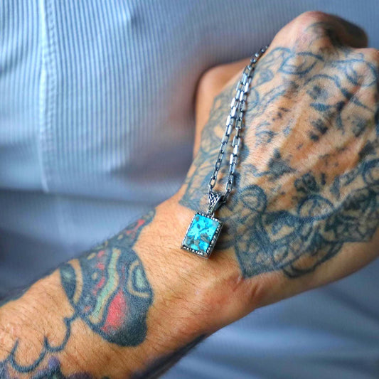 Close-up image of a handcrafted sterling silver ethnic necklace featuring a vibrant turquoise gemstone set in an intricately patterned round pendant, designed as a unisex accessory with vintage western charm and meaningful personalization options.