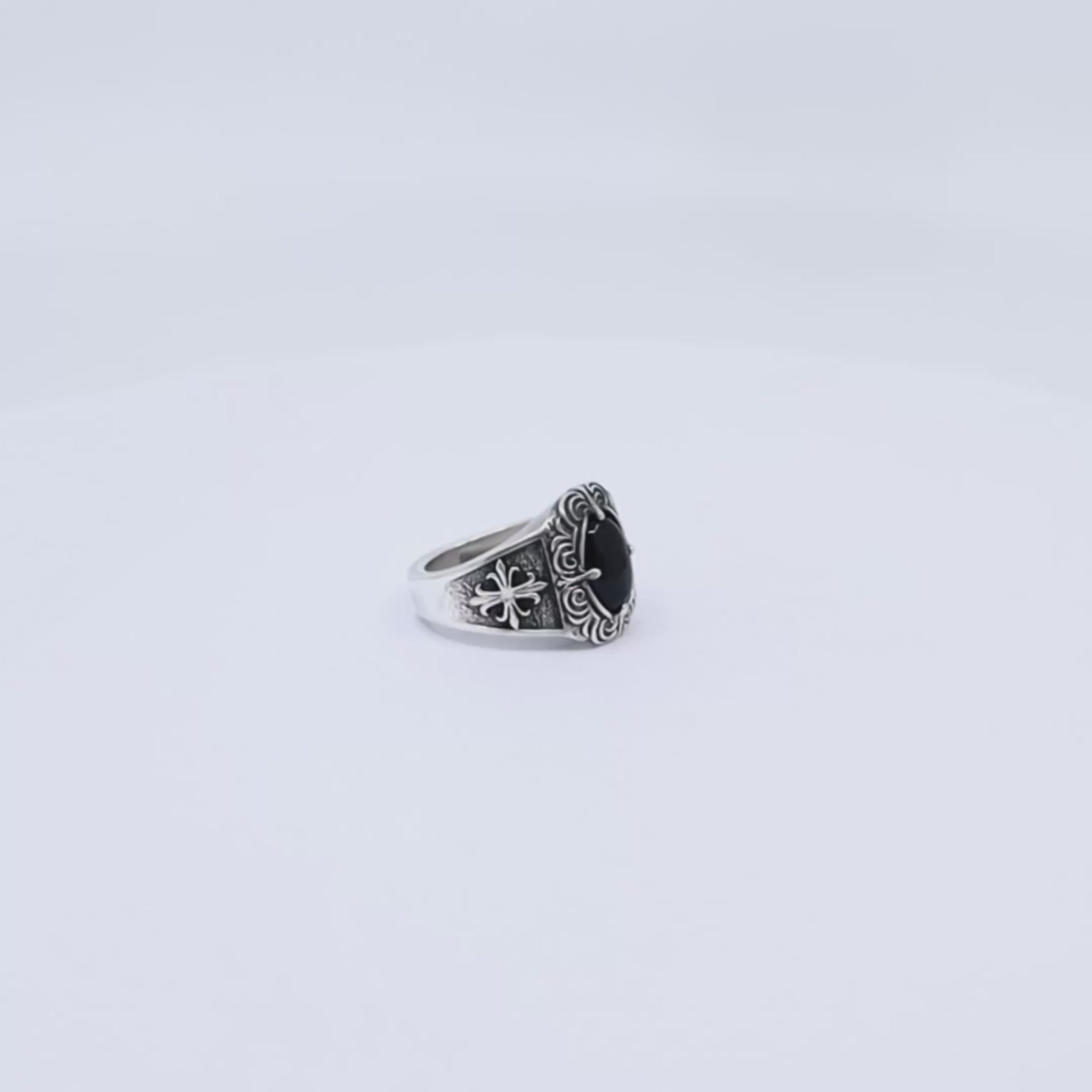 Artistic photograph of a vintage-inspired men's silver ring with a deep black onyx gemstone centerpiece, enriched with handcrafted gothic engravings and cross motifs on the band—perfect for gothic fashion lovers, biker aesthetics, or those looking for a unique, meaningful handmade gift.