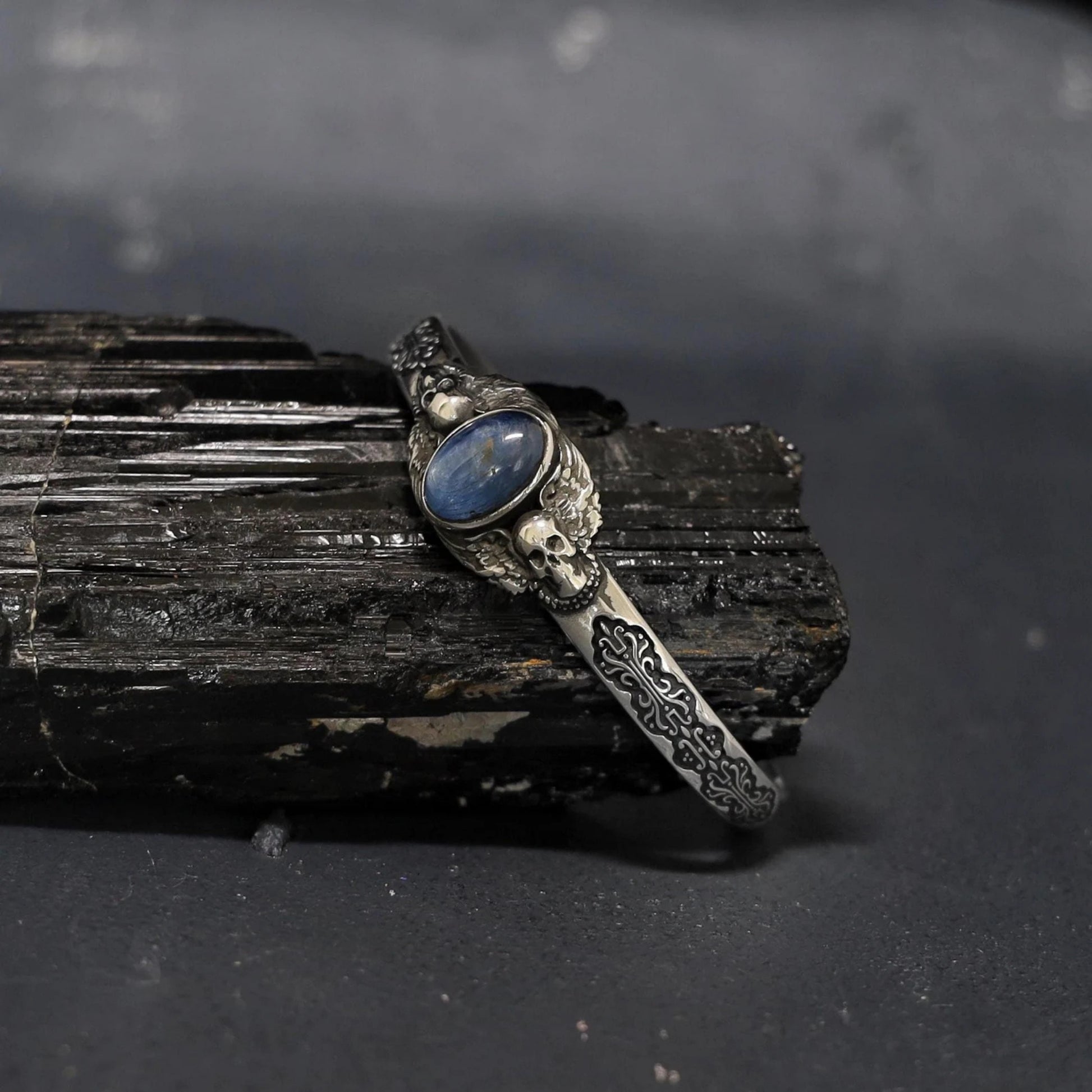 Artisan sterling silver bracelet for men with intricate skull engravings and oval blue kyanite centerpiece. Handmade using solid 925 silver, designed for gothic, biker, and vintage fashion enthusiasts seeking bold accessories.