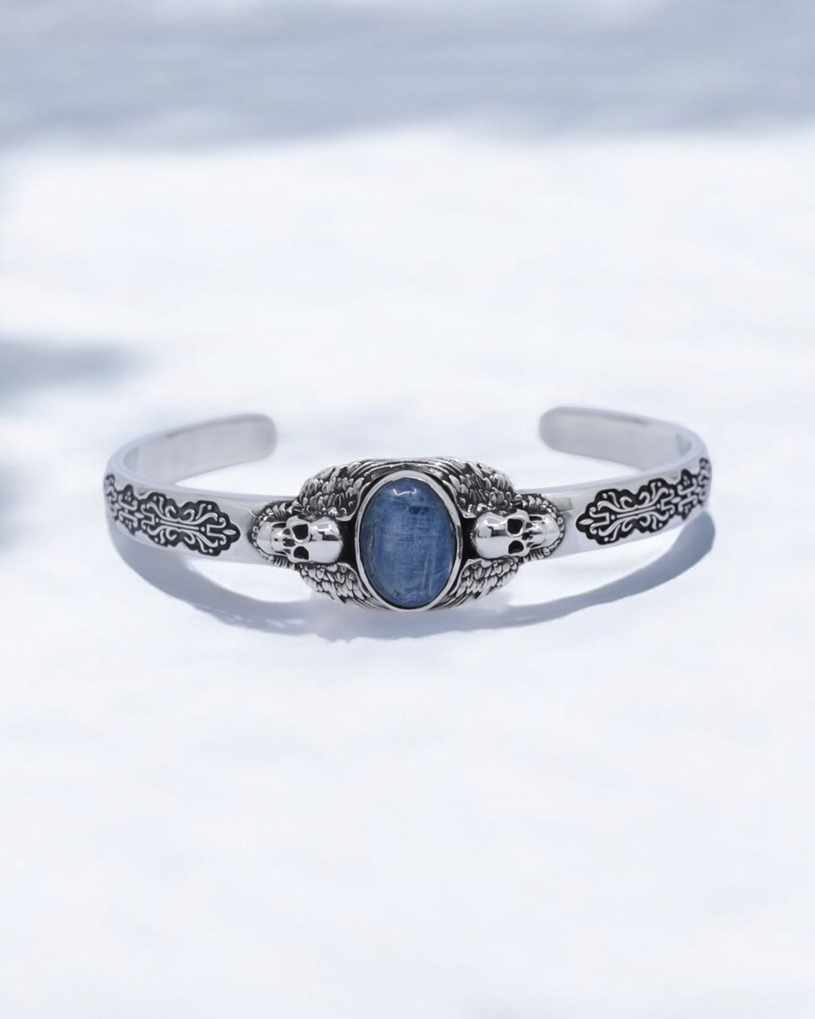 Close-up of handcrafted 925 sterling silver skull cuff bracelet featuring a natural blue kyanite gemstone in the center, surrounded by detailed gothic skull engravings and oxidized textures. Perfect for men who love handmade biker jewelry, unique gifts, and high-quality silver craftsmanship.
