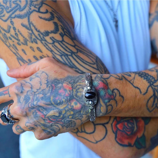 Detailed macro image of a men’s sterling silver cuff bracelet showcasing a natural black onyx stone. The skull motifs and oxidized silver texture reflect gothic artistry and bold masculine energy. Perfect gift for bikers and gothic jewelry lovers.