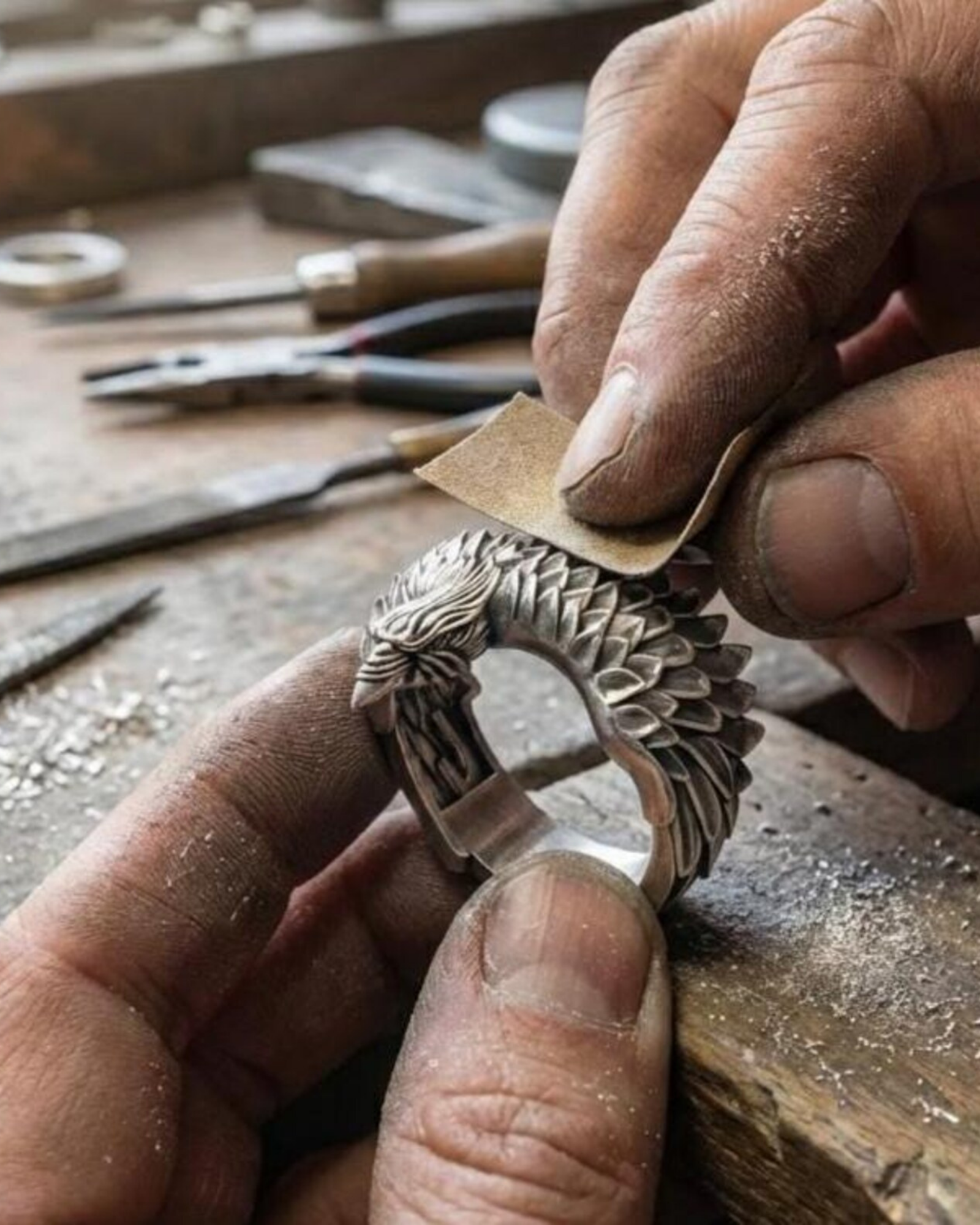 May include: A detailed, silver-colored ring featuring a carved eagle design. The eagle's wings are spread, and the ring has a textured surface. The ring is held in a hand, and the inside of the ring is marked with "925" and "Who".