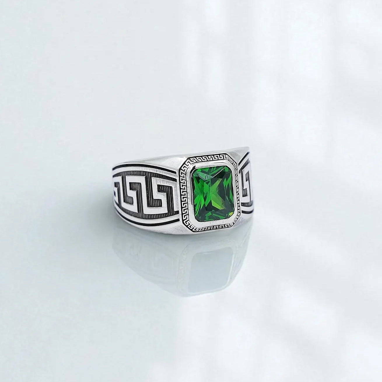 Front-facing view of a sterling silver men’s ring featuring an emerald-cut green gemstone framed by intricate Greek key patterns. This handcrafted statement ring blends classical Hellenistic symbolism with modern elegance, making it a perfect accessory for those who appreciate bold and refined jewelry.