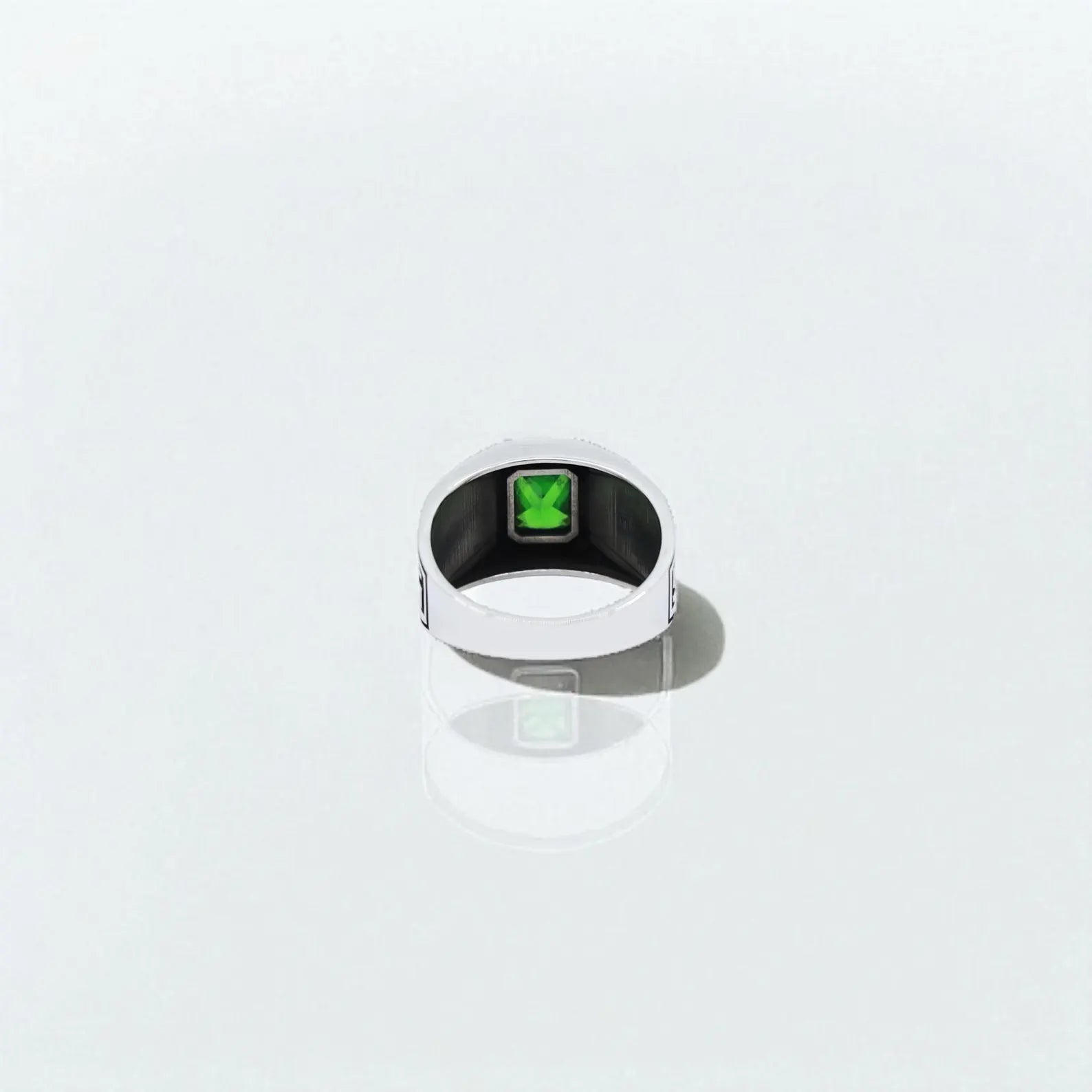 Diagonal close-up of a sterling silver men’s ring featuring an emerald-cut green stone set in a bold frame, surrounded by detailed Greek meander ornamentation. The elegant contrast between the polished silver and oxidized engravings enhances its timeless appeal, making it an ideal piece for men who value heritage-inspired statement jewelry.