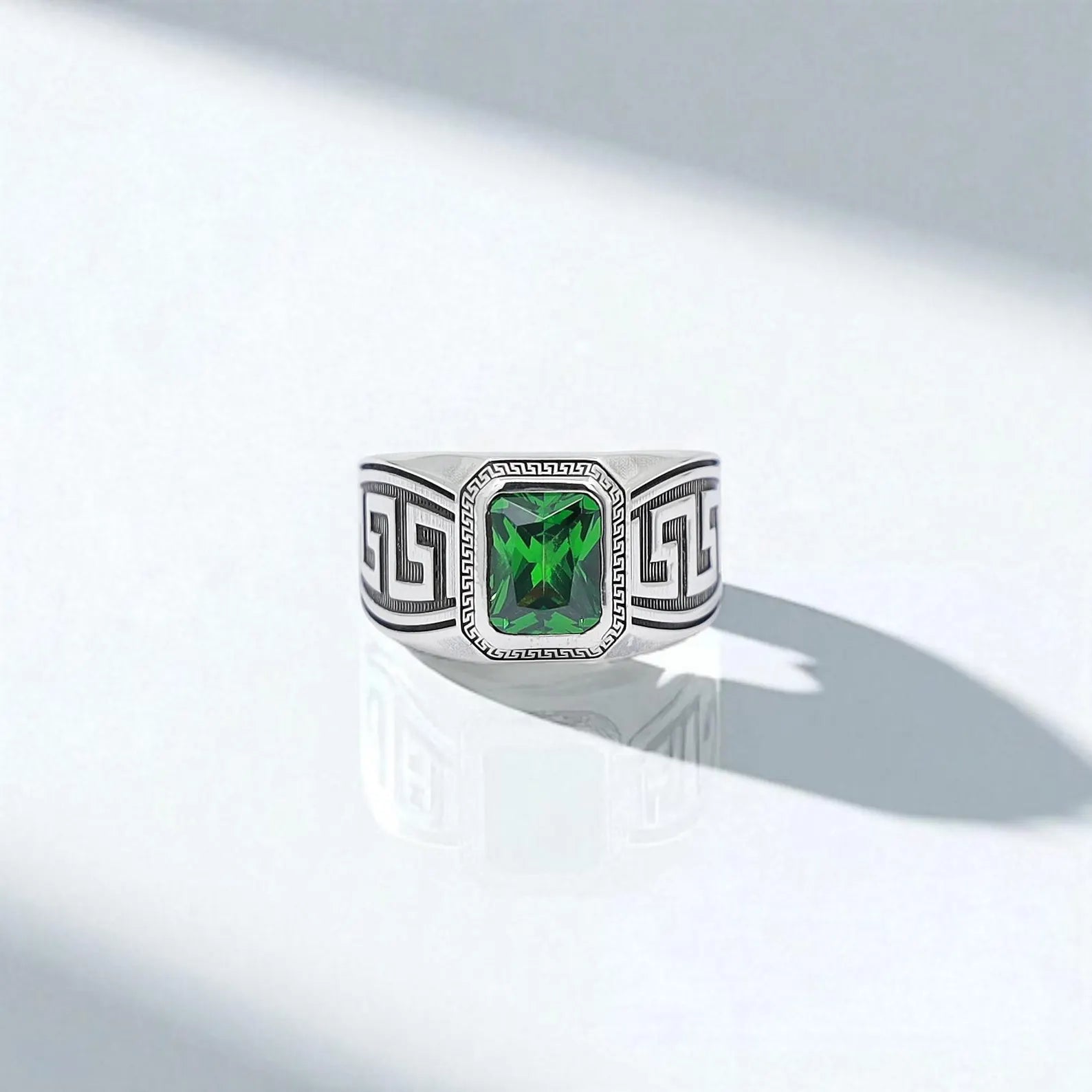 Top-down close-up of a men’s emerald-cut gemstone ring, showcasing the vibrant green center and detailed Greek meander engravings on either side. This ring represents unity, eternity, and personal strength — ideal for gifting or making a sophisticated fashion statement.