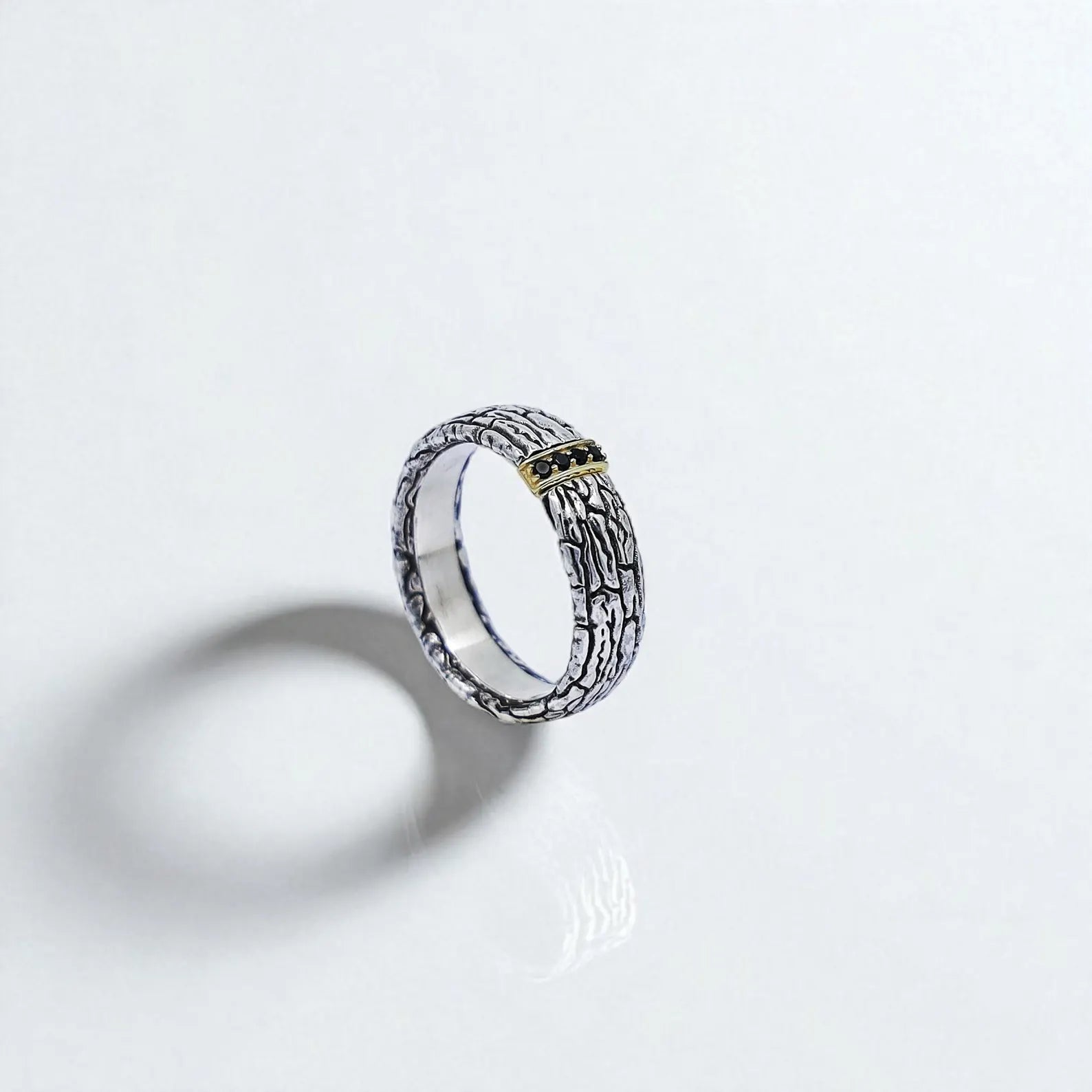Front-facing view of a handcrafted sterling silver band ring with a bark-like textured surface and a central gold-accented section set with black gemstones. This bold design combines rustic character and modern elegance, perfect for men who love unique and artistic statement jewelry.