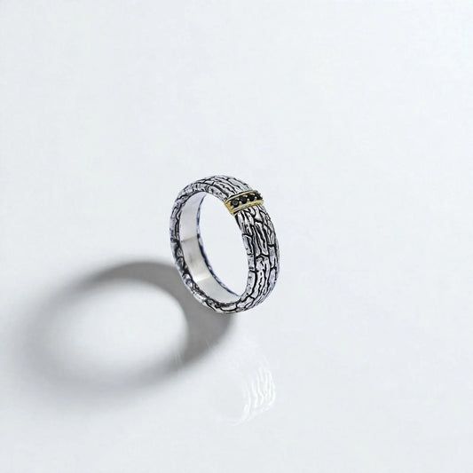 Front-facing view of a handcrafted sterling silver band ring with a bark-like textured surface and a central gold-accented section set with black gemstones. This bold design combines rustic character and modern elegance, perfect for men who love unique and artistic statement jewelry.