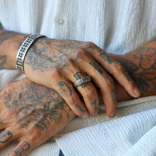 Close-up of a handcrafted sterling silver textured band ring for men, featuring elegant gold-plated accents and deep black gemstones set into the band, designed as a bold and luxurious statement piece that blends modern masculinity with artisan craftsmanship.