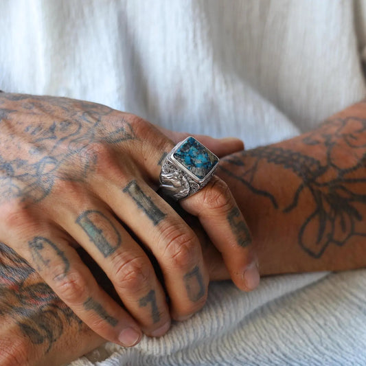 Artistic shot of a men’s handcrafted sterling silver ring with a bold square turquoise stone, paired with a flowing horse engraving on the band – representing wild spirit and masculine energy.