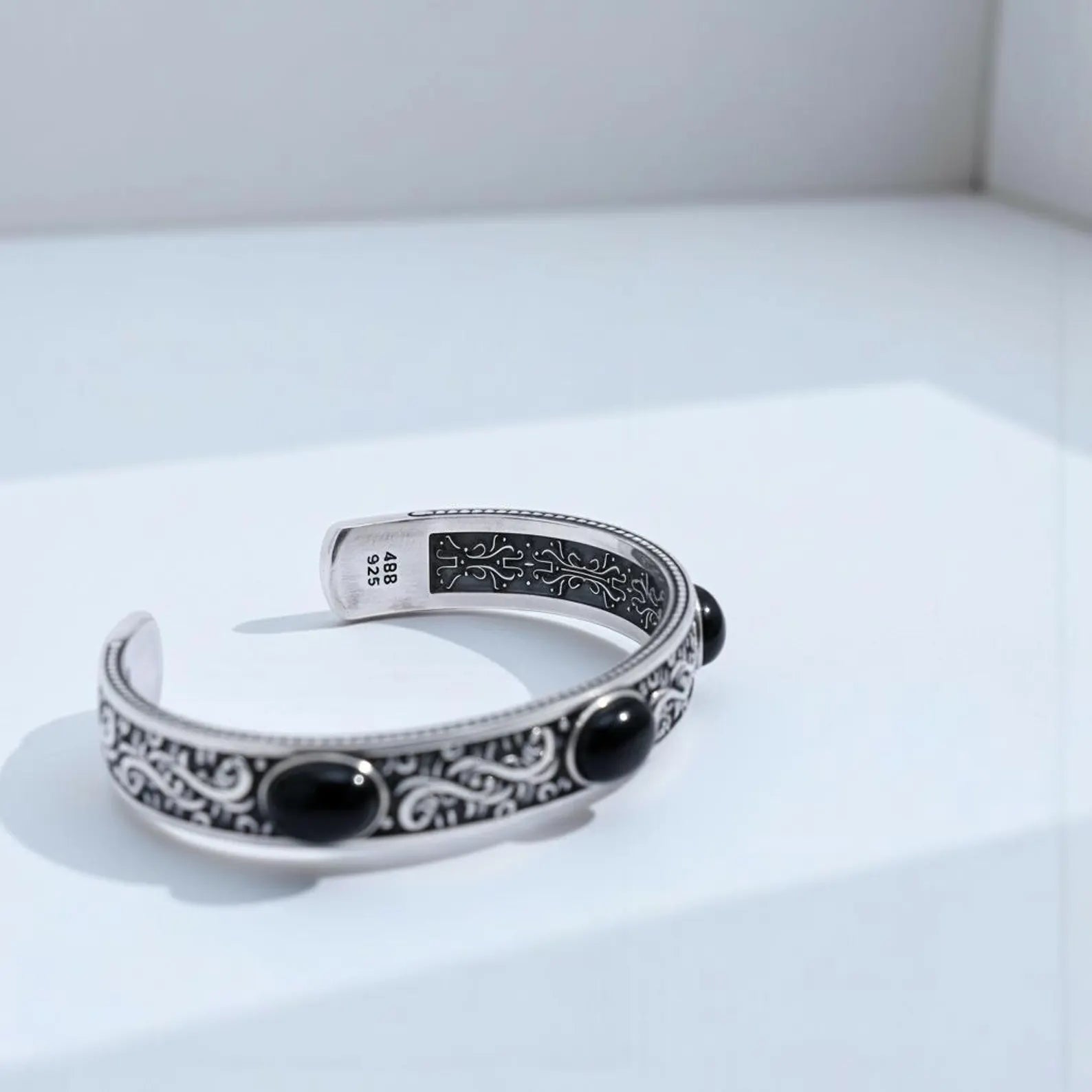 Elegant and bold onyx biker cuff bracelet with handcrafted sterling silver body, deep engraved motifs, and three natural onyx stones symbolizing grounding, strength, and protection.