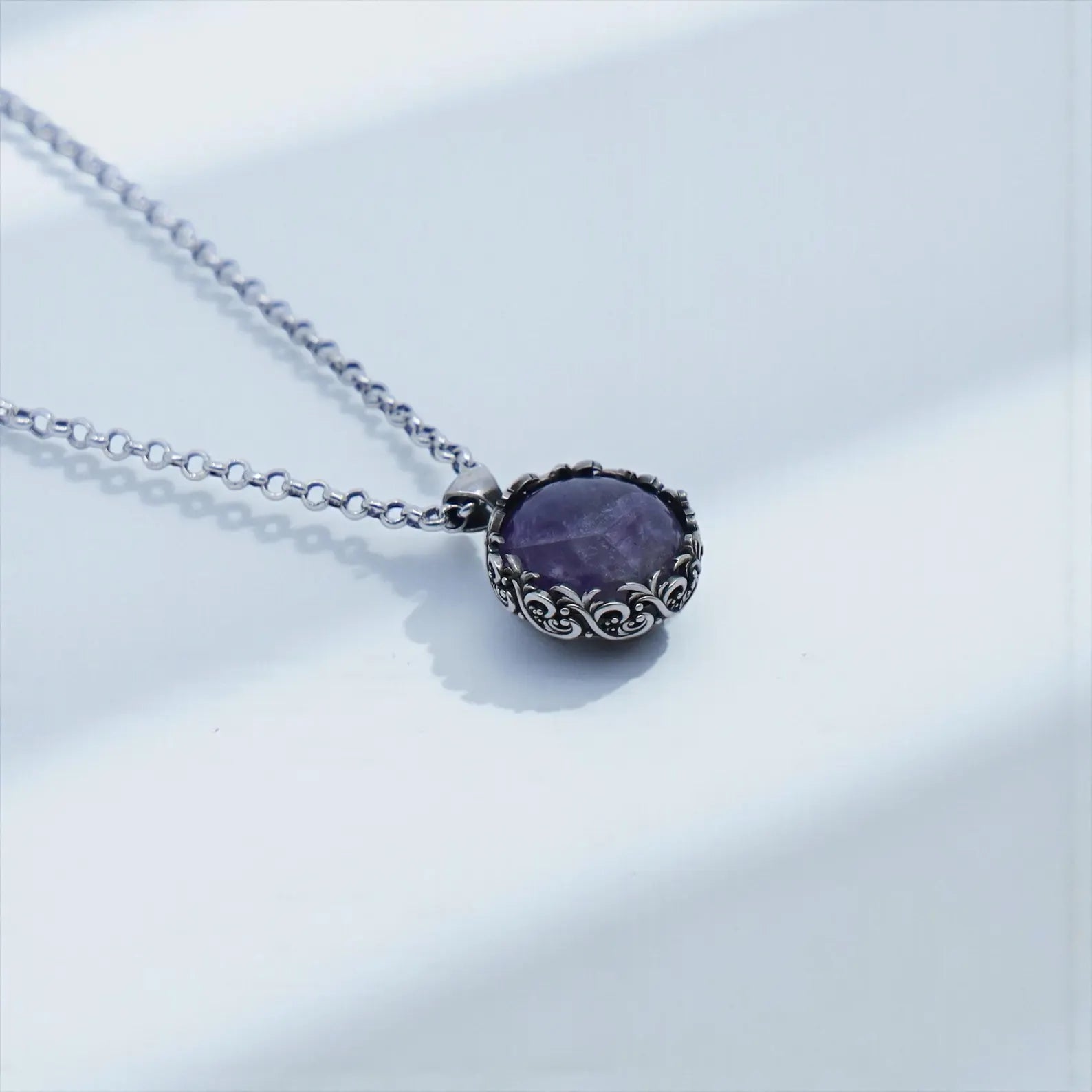 Detailed macro shot of a handcrafted sterling silver amethyst pendant with ornate baroque engravings, natural purple gemstone, oxidized finish, and premium artisan craftsmanship, ideal for statement jewelry collections.